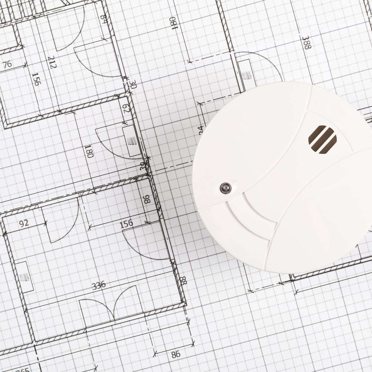 Smoke detector or fire alarm sensor on white architectural plans background, house safety or security concept, copy space, top view flat lay from above